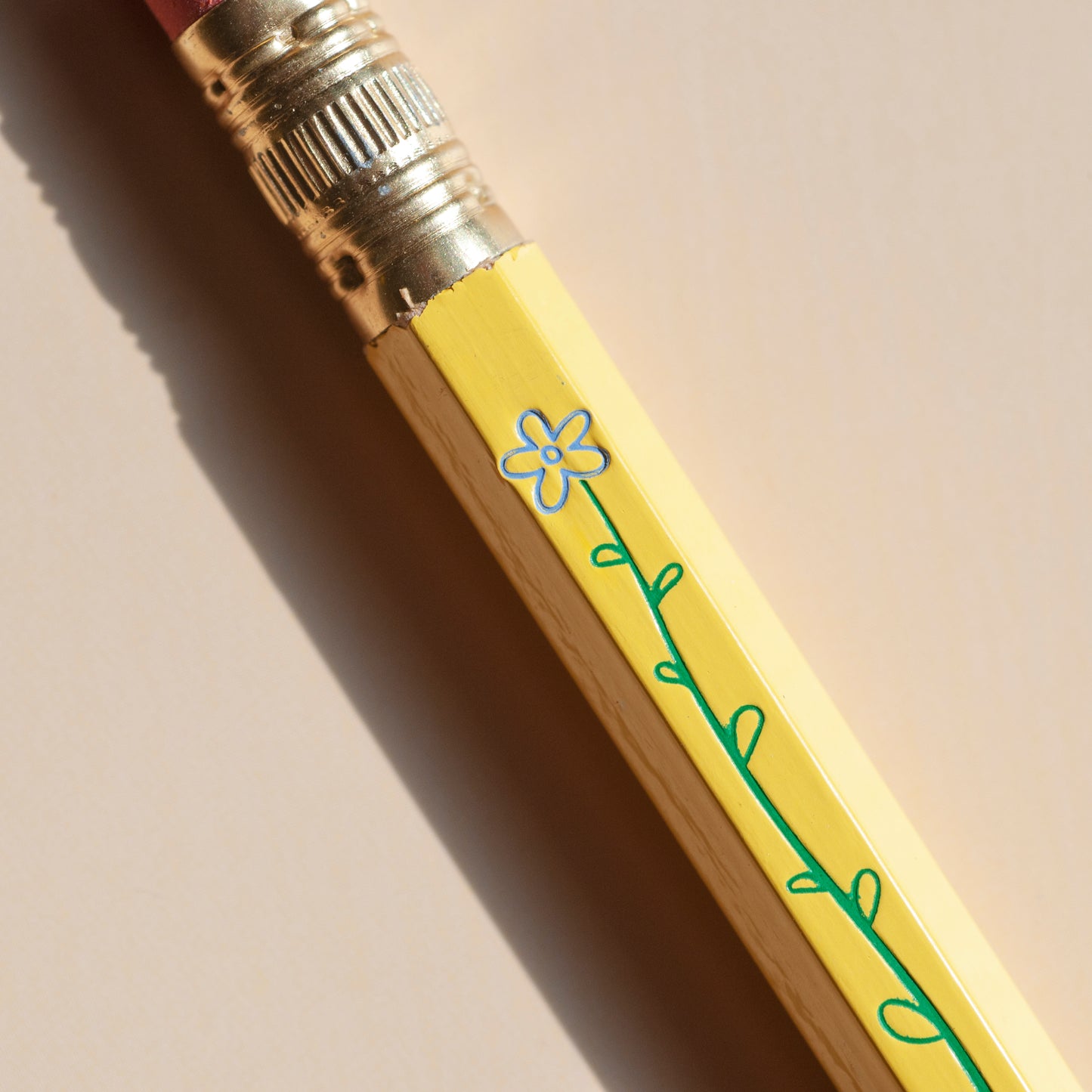 Macro shot of foil-stamped yellow pencil with blue flower and green stem