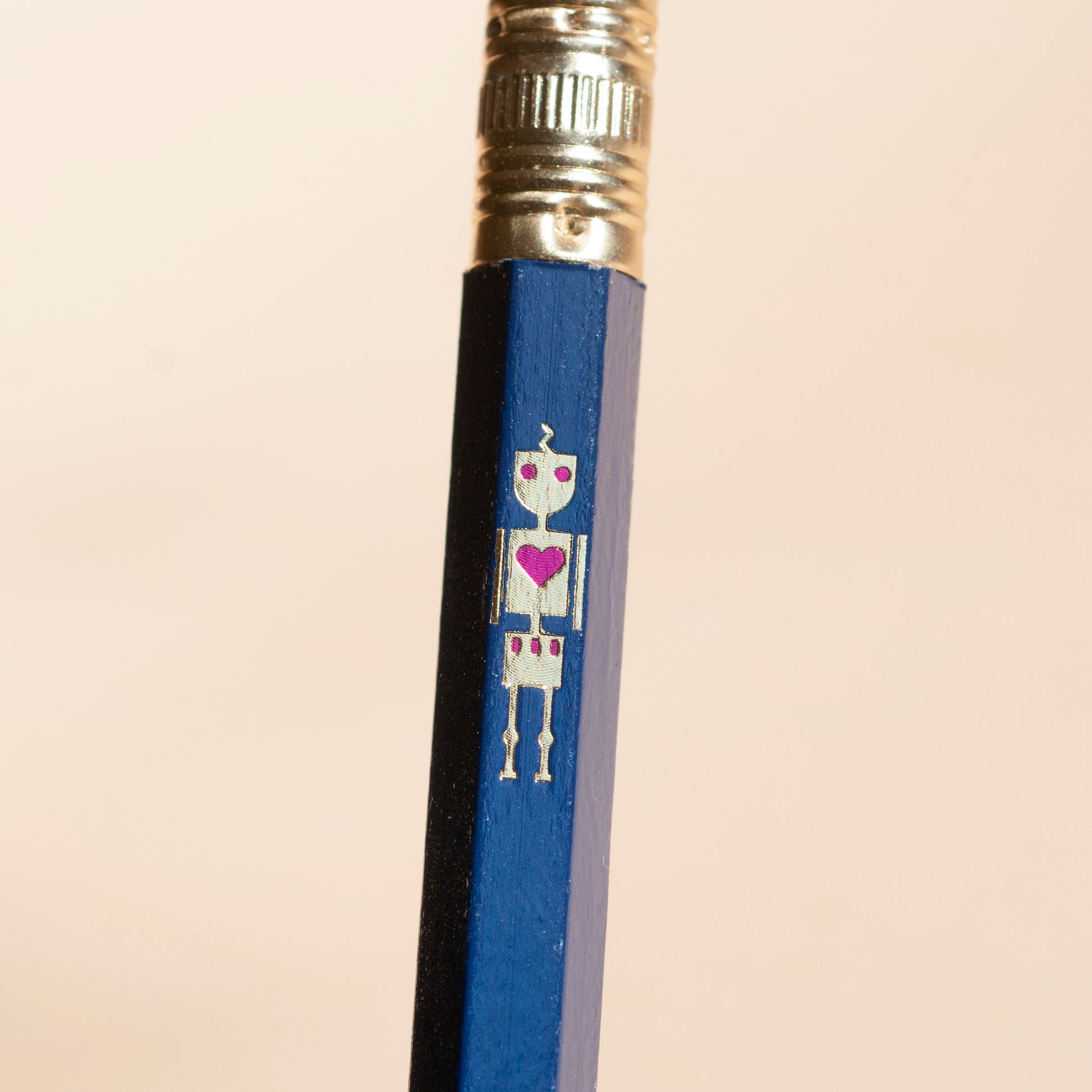 Macro shot of metallic gold foil robot design on a dark blue wooden pencil