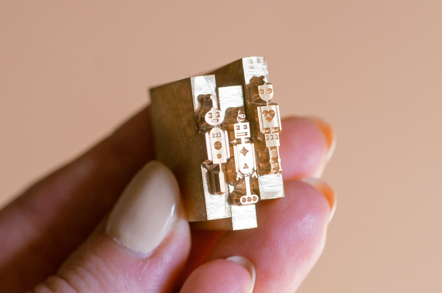 Tiny metal brass dies displaying robot shapes, made for hot-stamping machines that can stamp metallic foil designs onto wooden pencils